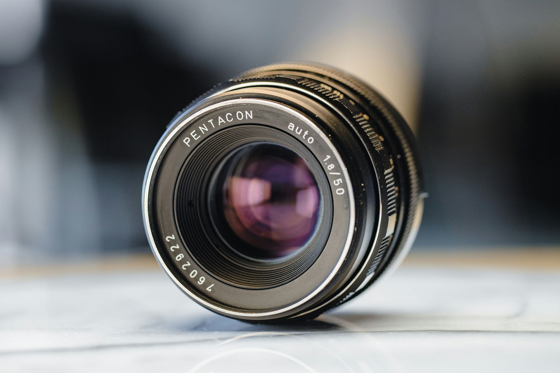 Ống kính Pentacon 50mm khẩu độ f/1.8 đặt trên bề mặt sáng, thể hiện thiết kế quang học cổ điển
